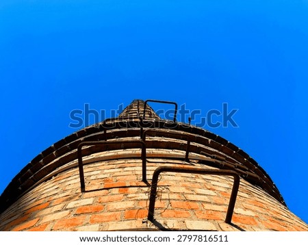 Close-up low angle view of the top of an old brick industrial chimney, against vivid blue sky
