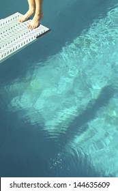 Closeup low section of a female diver standing backwards at the end of diving board over swimming pool