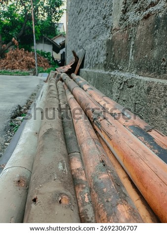 A close-up, low-angle shot of a bundle of old, stacked bamboo poles leaning against a rough concrete wall. Weathered texture and construction materials. Natural wood, tropical building, rustic texture