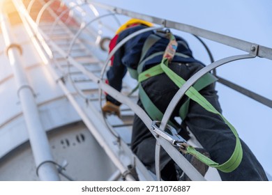 Close-up, low-angle shot of a construction worker in a safety harness climbing a cement silo ladder with sun flare, emphasizing safety protocols.