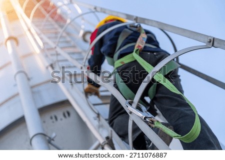 Close-up, low-angle shot of a construction worker in a safety harness climbing a cement silo ladder with sun flare, emphasizing safety protocols.