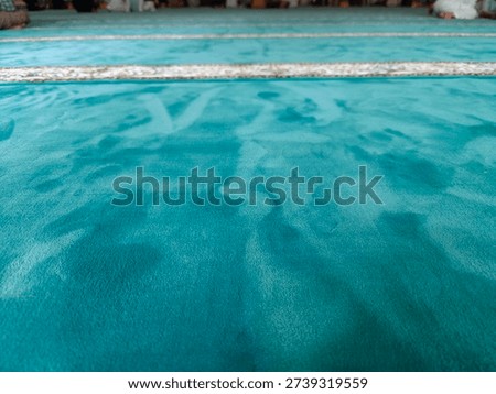 A close-up, low-angle shot of a textured surface, possibly a carpet or fabric, in varying shades of teal, blue, and green, creating an abstract and calming visual.
