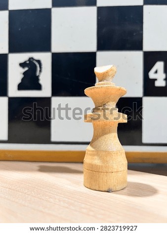 A close-up, low-angle shot of a worn set of light wooden chessmen lined up on a table. The focus is sharp on the natural wood grain and imperfections, most notably a chipped and broken knight in the center. The tall king and queen stand in the middle of the row, surrounded by pawns and other figures. In the blurred background, a large demonstration board is visible with a black knight silhouette and the number 