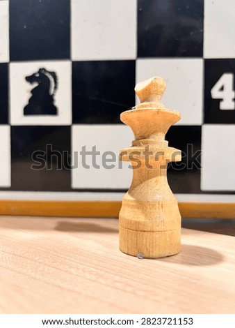A close-up, low-angle shot of a worn set of light wooden chessmen lined up on a table. The focus is sharp on the natural wood grain and imperfections, most notably a chipped and broken knight in the center. The tall king and queen stand in the middle of the row, surrounded by pawns and other figures. In the blurred background, a large demonstration board is visible with a black knight silhouette and the number 