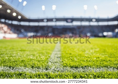 Close-up low-angle view of a white chalk boundary line on a vibrant green soccer pitch with a blurred stadium in the background.