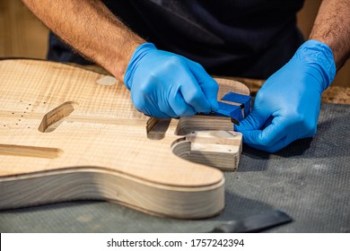 close-up of a luthier's hands at work on the body of a guitar, hands of a craftsman with protective gloves, music business and construction of musical instruments