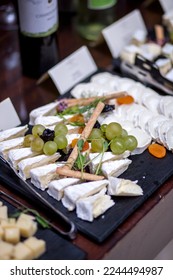 Closeup of luxurious fancy elegant European charcuterie board with brie, camembert and various cheeses with assorted colorful grapes and natural microgreen roots as toppings on dark platters - Shutterstock ID 2244494987