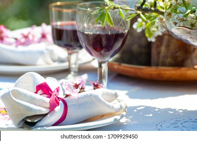 Close-up of luxury table setting for two on white linen rustic tablecloth in spring garden, outdoors . Two glasses with red wine on a table 