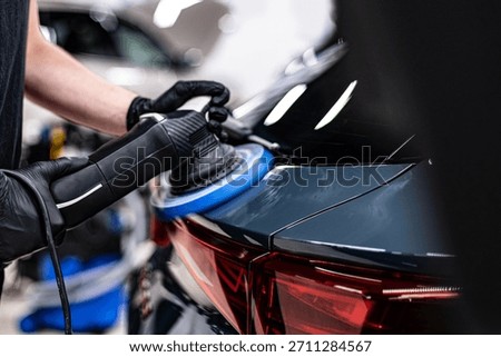 Close-up of machine polishing and paint correction on a car body panel near the rear taillight in a professional detailing studio, improving gloss, surface clarity and paint condition.
