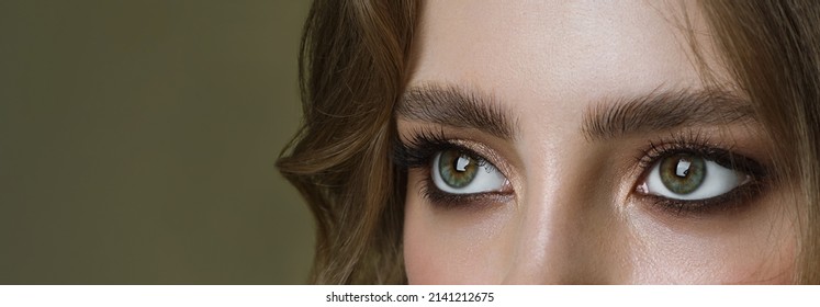 Close-up Macro Of A Beautiful Female Eye On Green Background With Perfect Shape Eyebrows. Clean Skin, Trendy Make-up, Looking Away Good Eyesight