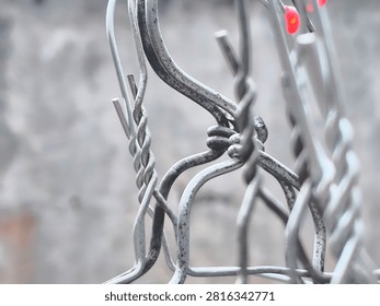 A close-up, macro shot of a complex wire joint where multiple metal wires are twisted and knotted together, serving as a connector in a fence or structure. The focus is sharp on the metallic texture, knots, and bends of the wires, while the background remains softly blurred, showing a neutral, industrial-themed environment. This image captures the technical detail and ruggedness of wire-based infrastructure. It is perfect for themes of construction, industrial engineering, metalworking, repairs, security fences, backyard structures, durability, craftsmanship, and raw materials. The image highlights the strength and utility of these simple but effective connections. Whether for commercial use, DIY tutorials, engineering documentation, or editorial content about urban environments and home maintenance, this photograph offers a clear, detailed, and visually engaging perspective on mundane but essential components of everyday infrastructure.