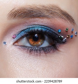 Closeup macro shot of human female brown color eye. Woman with natural evening vogue face beauty makeup. Girl with perfect skin, with blue eye shadow make up and rhinestones. - Shutterstock ID 2239428789