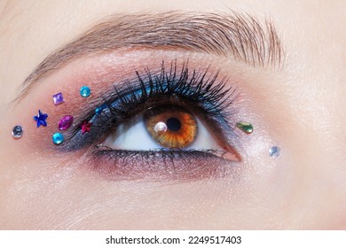 Closeup macro shot of human female brown color eye. Woman with natural evening vogue face beauty makeup. Girl with perfect skin, with blue eye shadow make up and rhinestones. - Shutterstock ID 2249517403