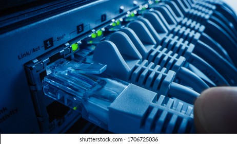 Close-up Macro Shot: Person Plugs in RJ45 Internet Connector into LAN Router Switch. Information Communication Network with Data Cable Being Connected to Port with Blinking Lights. Blue Background - Shutterstock ID 1706725036