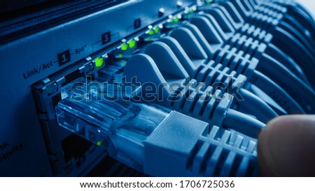 Close-up Macro Shot: Person Plugs in RJ45 Internet Connector into LAN Router Switch. Information Communication Network with Data Cable Being Connected to Port with Blinking Lights. Blue Background