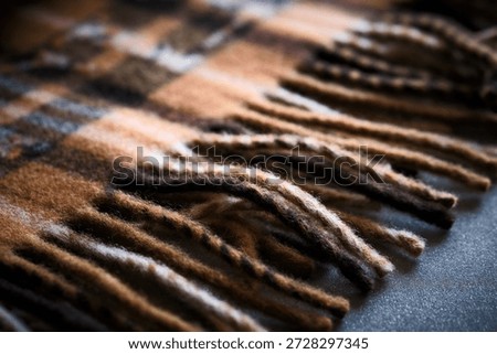 Close-up macro shot of warm wool scarf with soft fringes, lying on textured dark surface. Earthy colors and shallow depth of field create warm, tactile, autumn-inspired atmosphere