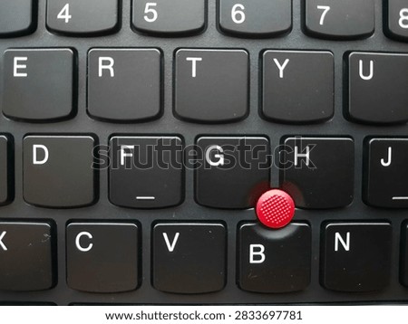 Close-up macro view of a black computer keyboard with a bright red trackpoint pointing device, highlighting modern technology and computer hardware.