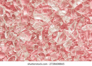 A close-up macro view of clear, broken glass pieces scattered across a soft pink background, creating a sparkling abstract texture with sharp geometric reflections. For background