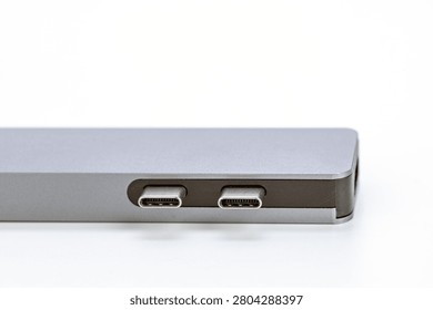 Close-up macro view of dual USB Type-C connector ports built into the brushed silver aluminum body of a sleek modern ultrabook laptop, highlighting modern connectivity standards on a clean white isolated studio background surface