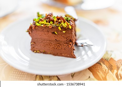 Closeup macro view of homemade layered pistachio chocolate raw vegan cake slice on white plate with chocolate shavings and nut green pieces texture