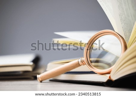 Closeup magnifying glass lean on the page of the opened book, research information, glossary, education concept