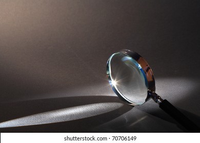 Closeup Of Magnifying Glass Standing On Dark Surface With Beam Of Light