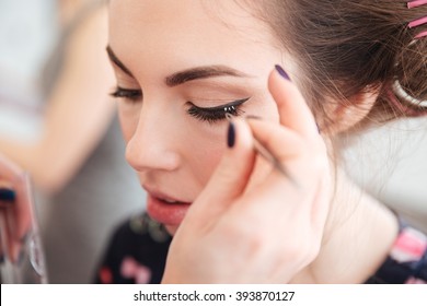 Closeup Of Makeup Artist Doing False Lashes To Young Woman In Curlers