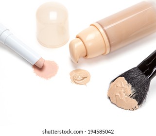 Close-up Of Makeup Concealer Pencil, Foundation With Open Jar And Makeup Brush On White Background