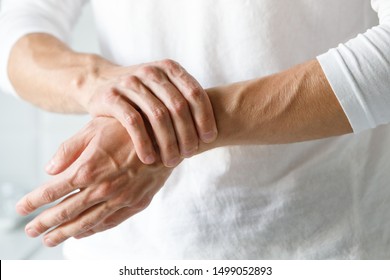 Closeup of male arms holding his painful wrist caused by prolonged work on the computer, laptop. Carpal tunnel syndrome, arthritis, neurological disease concept. Numbness of the hand - Shutterstock ID 1499052893