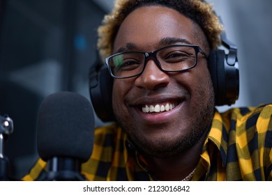 Close-up of a male blogger wearing headphones, speaking into a microphone, recording a podcast in the studio. Portrait of smiling black man. Modern technologies, equipment and the concept of blogging