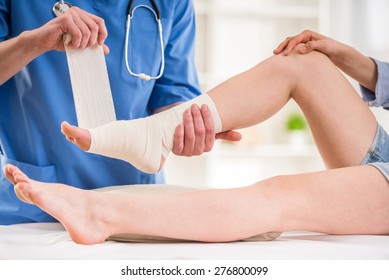 Close-up of male doctor bandaging  foot of female patient at doctor's office.