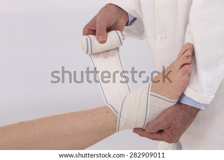Close-up of male doctor bandaging foot of female patient at doctor's office.