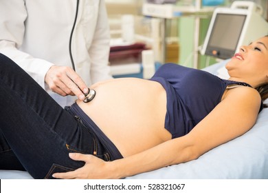 Closeup of a male doctor using a stethoscope to examine a pregnant woman in a hospital