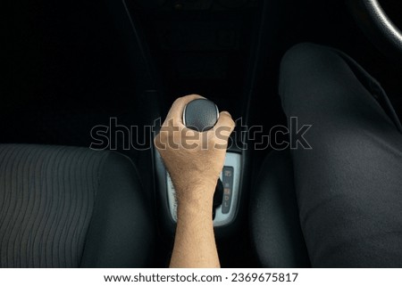  Close-up of male driver's hands changing the automatic transmission lever of the car. Top view of man's hand holding automatic transmission inside car to drive forward.