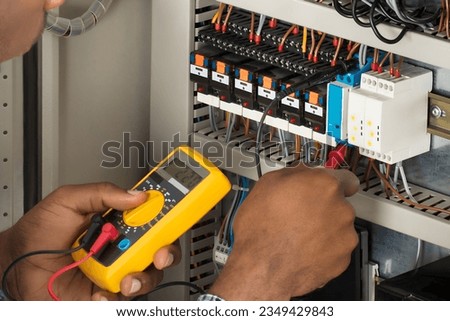 Close-up Of Male Electrician Checking Fuse Box With Multimeter