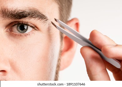 Close-up Of Male Eye And Tweezers For Eyebrow Grooming And Shape Correction