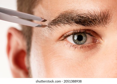 Close-up Of Male Eye And Tweezers For Eyebrow Grooming And Shape Correction