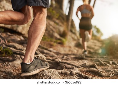 Closeup of male feet run through rocky terrain. Cross country running with focus on runner's legs.