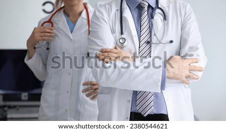 Close-up of male and female doctors standing in hospital office. Man standing with crossed arms and woman holding stethoscope. Doctors wearing white medical gowns