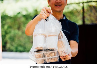 Close-up Of Male Food Delivery Man On Service Job Giving Foods Of Bubble Tea, Coffee, Lunch Box At Home