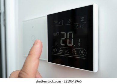 Close-up of a male hand adjusting a modern wall-mounted digital thermostat. 20 degrees Celsius room comfortable temperature. electronic thermometer on the wall