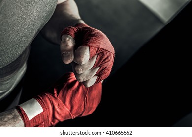 Closeup male hand of boxer with red boxing bandages. Fists of fighter before the fight or training in sport gym.