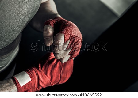Closeup male hand of boxer with red boxing bandages. Fists of fighter before the fight or training in sport gym.
