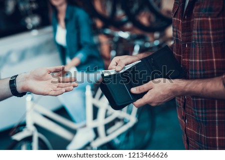Closeup of Male Hand Gives Money From Purse to Seller. Shop Assistant Hand Takes Cash with Blurred Customers and Bikes on Backround in Sport Bicycle Store. Cash Payments Concept