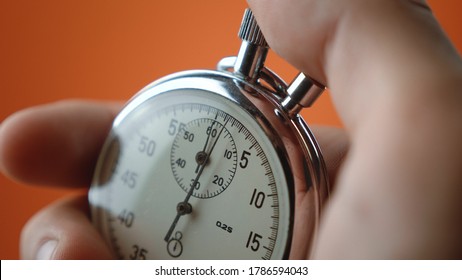 Close-up of male hand holding analogue stopwatch on orange background. Time start with old chronometer man presses start button in the sport concept. Time management concept. - Shutterstock ID 1786594043