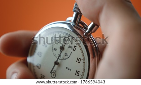 Close-up of male hand holding analogue stopwatch on orange background. Time start with old chronometer man presses start button in the sport concept. Time management concept.