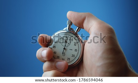 Close-up of male hand holding analogue stopwatch on blue background. Time start with old chronometer man presses start button in the sport concept. Time management concept.