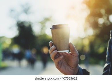 Close-up of male hand holding coffee to take away at early morning in park, flare light 
