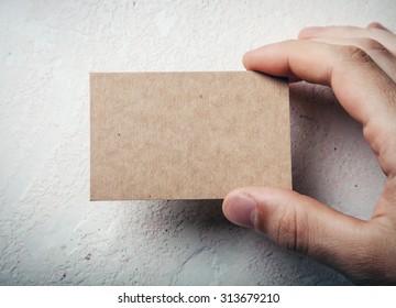 Closeup Of Male Hand Holding Craft Business Card On Concrete Wal