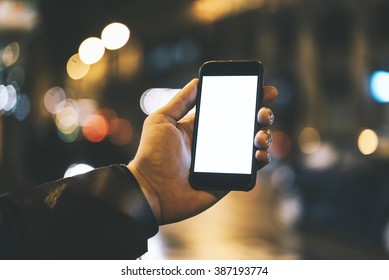Closeup of male hand holding modern smartphone with blank screen for your text message or content, man's hand using cellphone with empty display at night city, bokeh light - Powered by Shutterstock